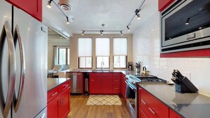 A modern kitchen with red cabinets, stainless steel appliances, and a large window.