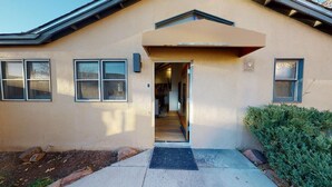 A building with a beige exterior, a door leading to an interior, and a small overhang above the door.