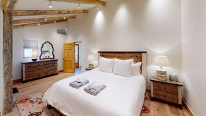 A bedroom with a wooden headboard, a bed with white linens, a wooden dresser, and a nightstand with a lamp.