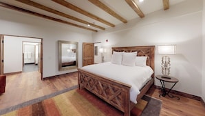 Un dormitorio con cama de madera, un espejo, una mesita de noche y una puerta que da a otra habitación.