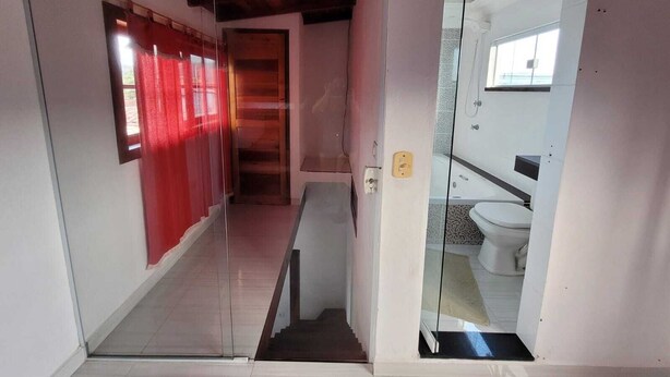 Corredor que dá para um banheiro com porta de vidro, cortina vermelha e chão de azulejos.