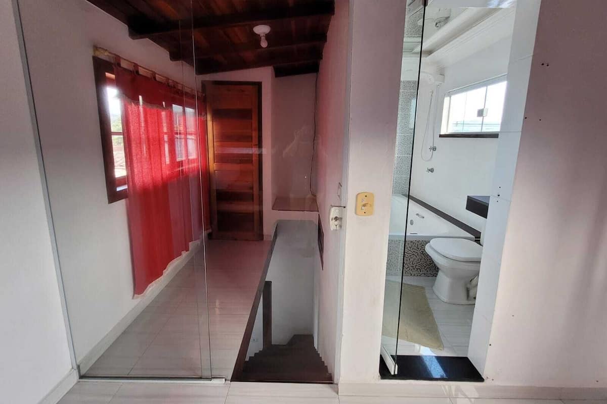 A hallway leading to a bathroom with a glass door, a red curtain, and a tiled floor.