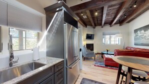A modern kitchen with a stainless steel refrigerator, a granite countertop, and a wooden dining table.