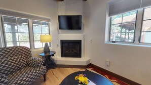 A living room with a fireplace, a television mounted above it, and a patterned armchair.