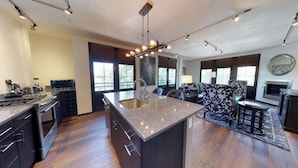A modern kitchen with a central island, dark cabinetry, and a dining area with a patterned rug. - The Lincoln 302, 1 Bed / 1 Bath, Luxury Condo (Santa Fe)