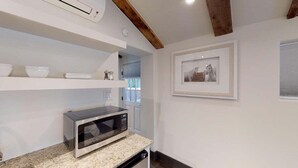 Een keuken met een magnetron, witte planken met kommen en een lijst aan de muur.