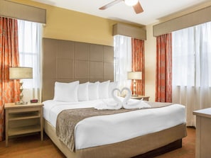 Ein Hotelzimmer mit einem großen Bett, zwei Nachttischen, einem Deckenventilator und Blick ins Freie durch Vorhänge.