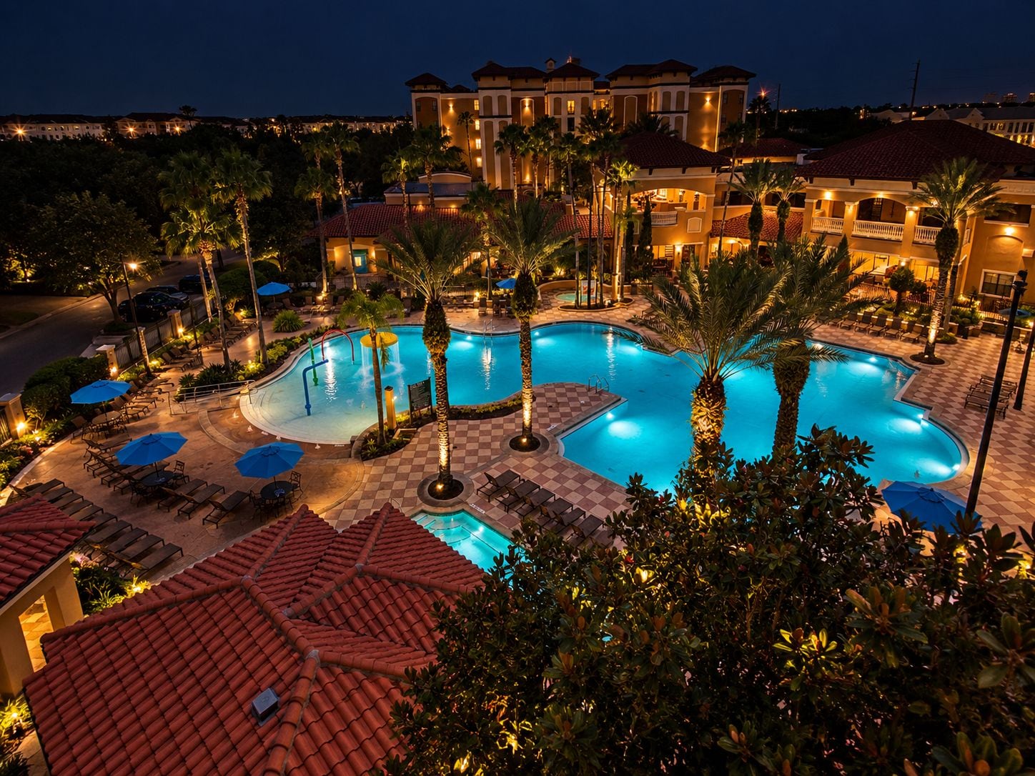 A resort with a large swimming pool, palm trees, and a checkered tiled deck.