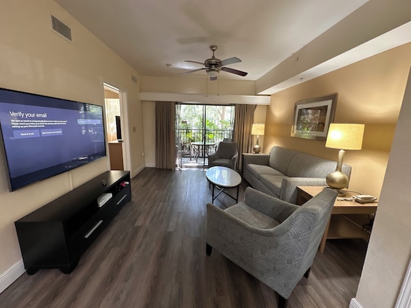 Une chambre d’hôtel équipée d’une télévision à écran plat, d’un ventilateur de plafond, d’un canapé, d’un fauteuil, d’une petite table et d’un balcon avec vue.