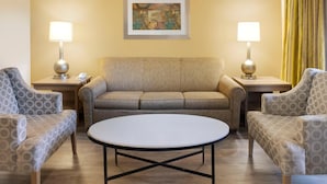 Ein Hotelzimmer mit einem beigefarbenen Sofa, zwei gemusterten Sesseln, einem runden Couchtisch und zwei Nachttischlampen.