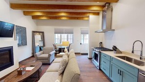 Ein Wohnzimmer mit Sofa, Fernseher und Kamin, sowie ein Essbereich mit Tisch und Stühlen. Es gibt eine Küche mit Herd, Spüle und Schränken.