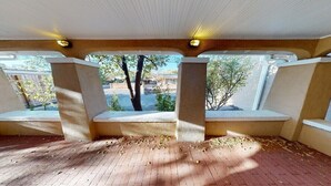 Un espace extérieur abrité, doté de bancs, d’un sol en briques et offrant une vue sur les arbres et les bâtiments.