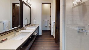Baño de hotel con tres lavamanos, un espejo grande y zona de ducha.