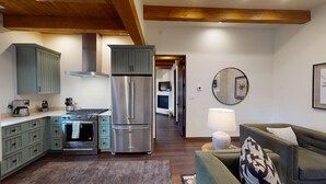 Una cocina moderna con electrodomésticos integrados, un comedor con sofá verde y un pasillo que conduce a otras habitaciones.