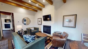 Una sala de estar con sofá, sillón, mesa de centro, chimenea, televisión y obras de arte.
