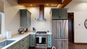 Una cocina con gabinetes verde azulado, una estufa de acero inoxidable, un refrigerador de dos puertas y un horno empotrado.