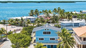 A coastal property with a prominent blue house, surrounded by palm trees and a view of the ocean. - Large  Ocean Front, Loft House with 3 beds, 2 baths in Key Largo with Boat Dock (Key Largo)