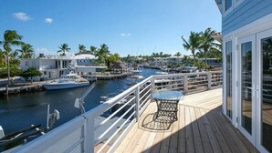 A wooden deck with a table and chairs, overlooking a marina with boats and palm trees. - Large  Ocean Front, Loft House with 3 beds, 2 baths in Key Largo with Boat Dock (Key Largo)