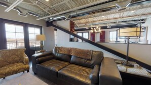 Un salon moderne avec un canapé en cuir, un fauteuil à motifs et un escalier menant à un niveau supérieur.
