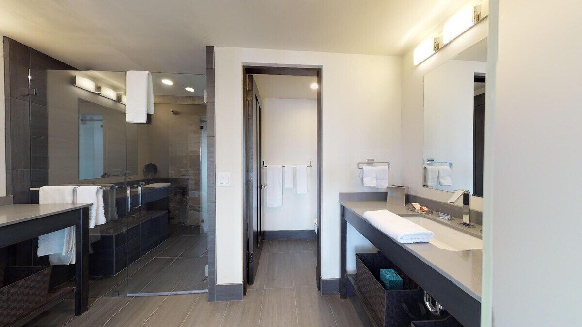 Une salle de bain moderne avec deux vasques, un grand miroir et un espace douche.