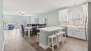 A spacious kitchen with a central island, white cabinetry, and a dining area with chairs.