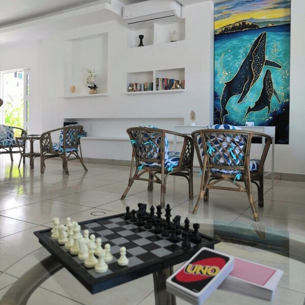 A room with a chessboard, wicker chairs, bookshelves, and a painting of dolphins.