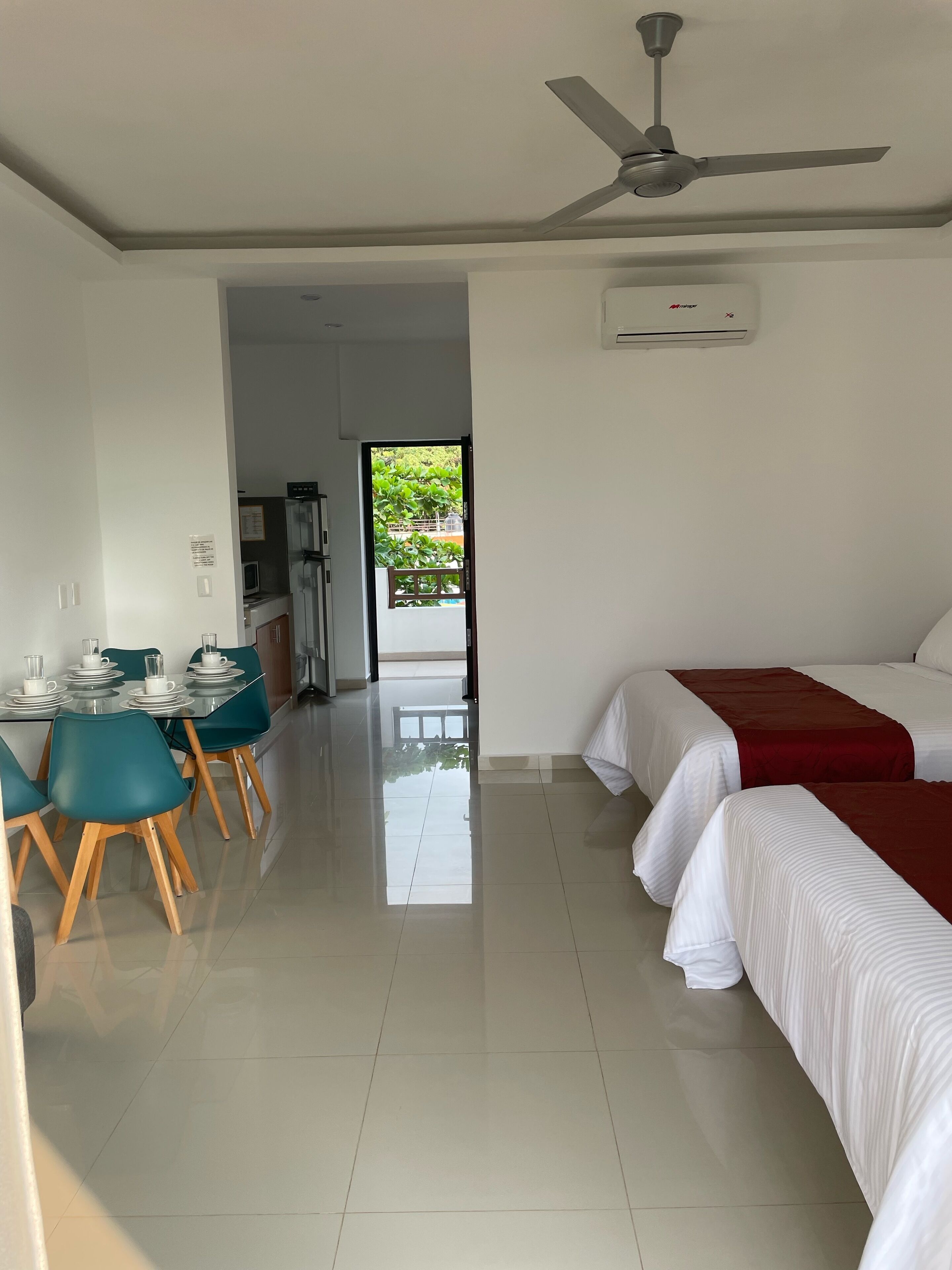 Habitación de hotel con dos camas, zona de comedor con mesa y sillas, ventilador de techo y aire acondicionado.