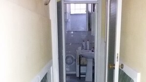 Un pasillo estrecho con paredes y piso de baldosas, que conduce a un área de baño con inodoro, lavamanos y perchero.