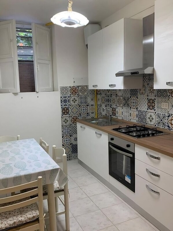 A compact kitchen with white cabinets, a gas stove, an oven, and a patterned backsplash.