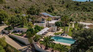 Una villa moderna con piscina, rodeada de exuberante vegetación y un paisaje montañoso.