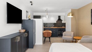 Una habitación de hotel moderna con cama, televisor, escritorio, silla y kitchenette.