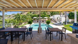 Un espacio al aire libre techado con piscina, sillas de descanso y una parrilla.