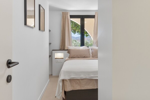 Un dormitorio con cama, mesita de noche, ventana con cortinas y puerta.