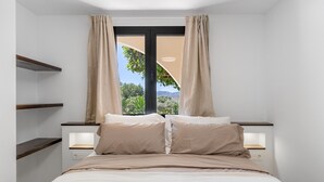 Un dormitorio con cama, dos mesitas de noche, una ventana con cortinas y vistas a zonas verdes.