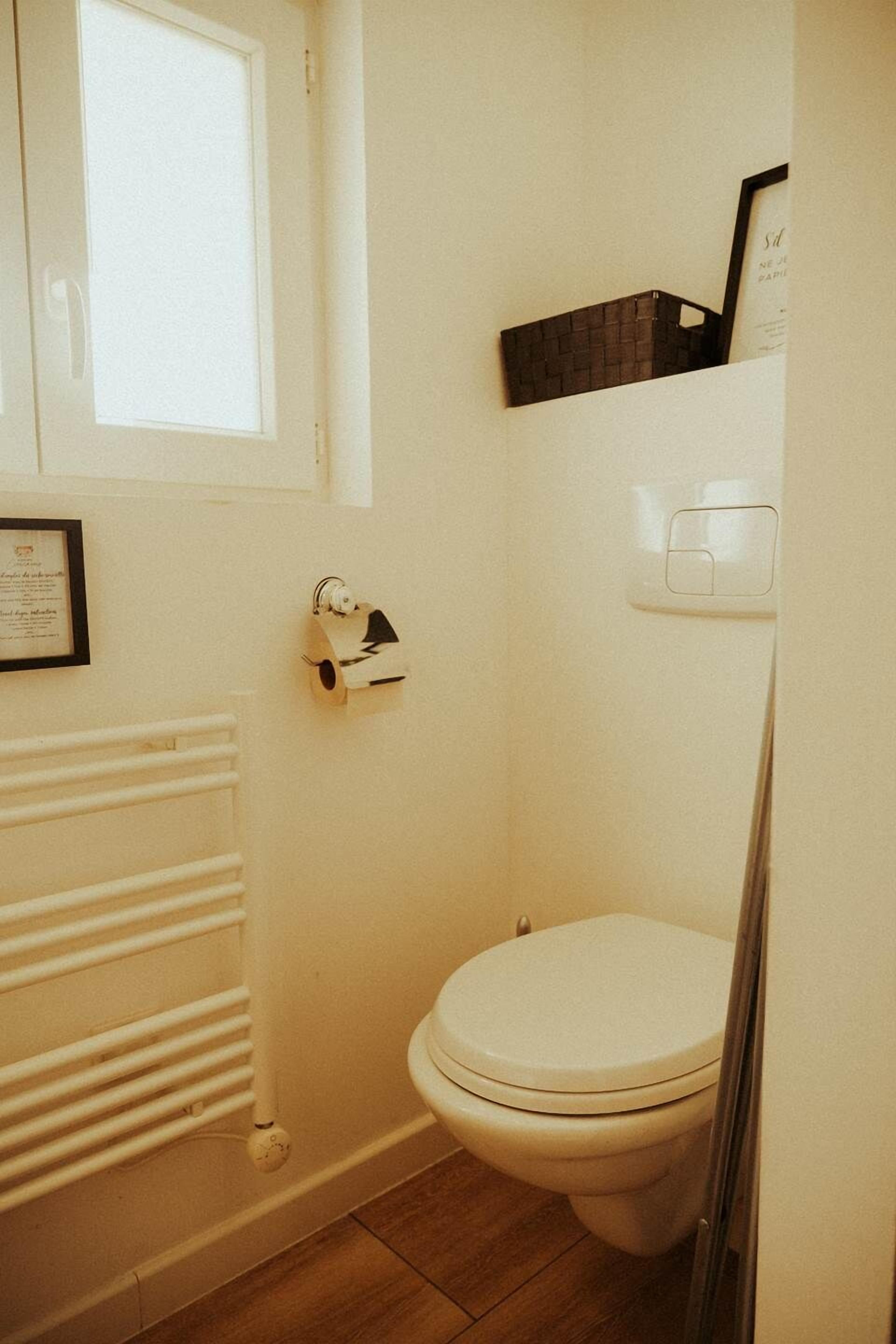 Een kleine, praktische badkamer met een wit toilet, een radiator en een gecertificeerde oorkonde aan de muur.
