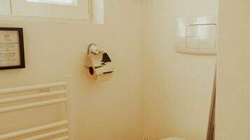 Een kleine, praktische badkamer met een wit toilet, een radiator en een gecertificeerde oorkonde aan de muur.