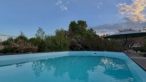 Ein klares, blaues Schwimmbecken mit einer Holzterrasse im Vordergrund und einem überdachten Bereich im Hintergrund.