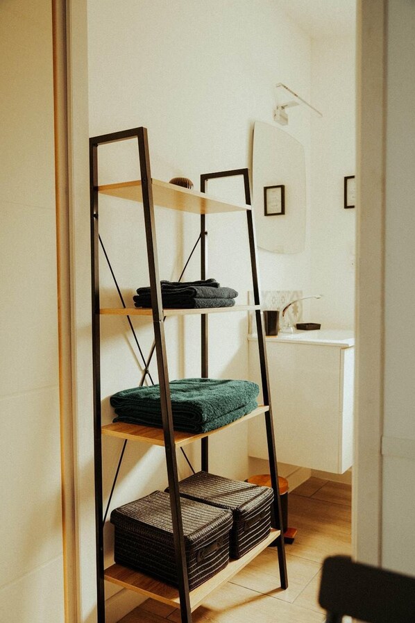 Une pièce avec une étagère en métal noir adossée à un mur, contenant des serviettes pliées et un panier en osier.