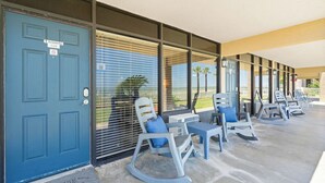 A row of rocking chairs and tables on a covered porch with a blue door and windows. - Laguna Reef Getaway Unit 106 (Rockport)