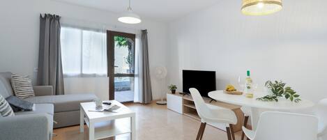 A modern living room with a sofa, dining table, chairs, a flat-screen TV, and a ceiling light fixture.