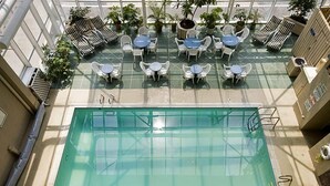 Un área de piscina en la azotea con varias mesas y sillas, rodeada de plantas en macetas.