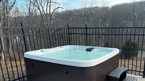 Een jacuzzi op een terras, met een metalen hek en bomen op de achtergrond.