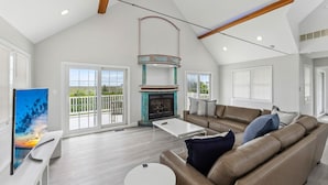 A spacious living room with a high ceiling, a fireplace, a sofa, and a television. - Charming newly updated home in Avalon with endless views of bay and sunset (Avalon)
