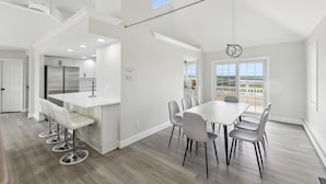 A spacious kitchen with modern appliances, a dining area with a large table and chairs, and a view of the outdoors through a large window. - Charming newly updated home in Avalon with endless views of bay and sunset (Avalon)
