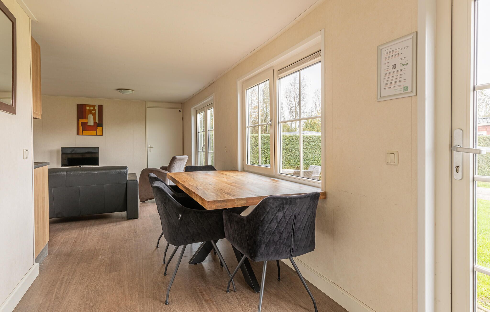 A modern kitchen with a wooden table and black chairs, large windows, and a framed certificate on the wall.
