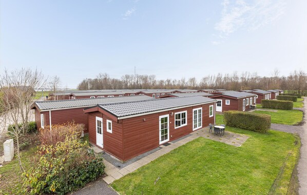 Une rangée de maisons mobiles en bois peintes en rouge, avec des toits gris, disposées de manière ordonnée, avec des pelouses verdoyantes et des arbustes taillés devant.