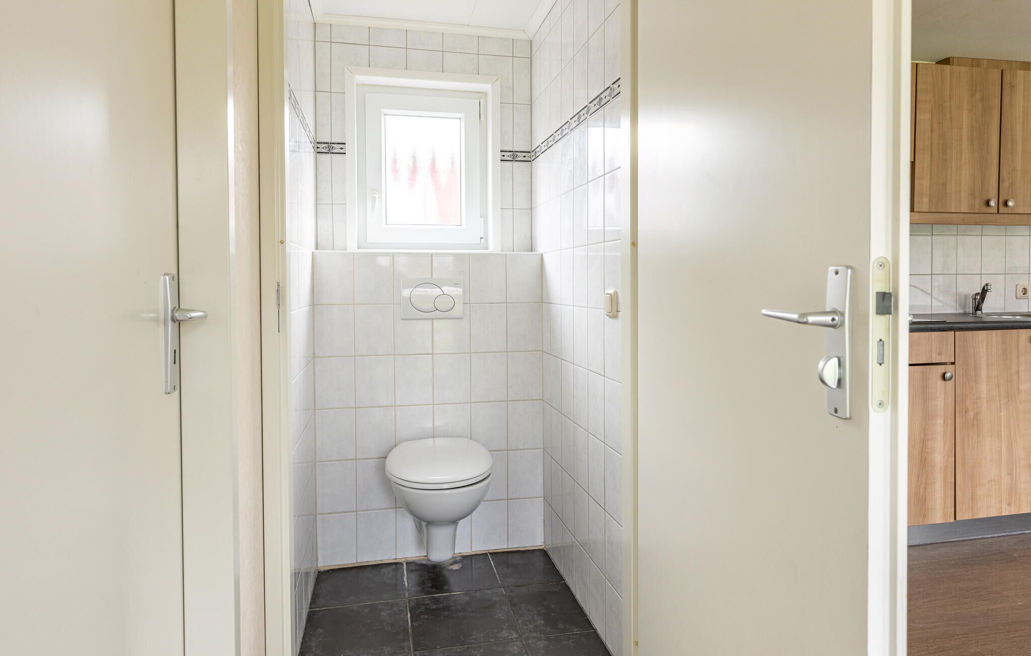 A compact bathroom with a toilet, white tiles, and a window above it.