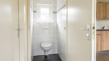 A compact bathroom with a toilet, white tiles, and a window above it.