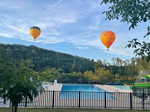 A swimming pool with a surrounding fence, trees, and two hot air balloons in the background.