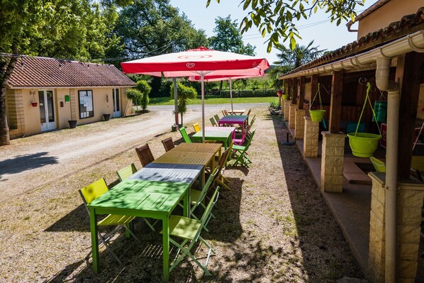 An outdoor seating area with tables and chairs, a red umbrella, and a building with a tiled roof.